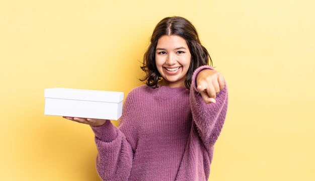 Joven hispana apuntando a la cámara eligiéndote. concepto de caja en blanco