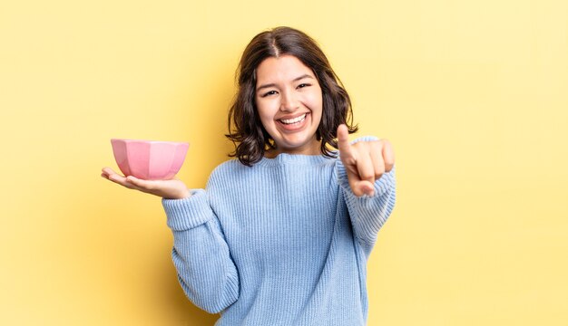 joven hispana apuntando a la cámara eligiéndote. concepto de cuenco vacío