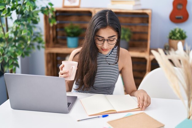 Joven hispana bebiendo café estudiando en casa