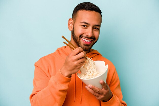 Joven hispana comiendo fideos aislado sobre fondo azul.