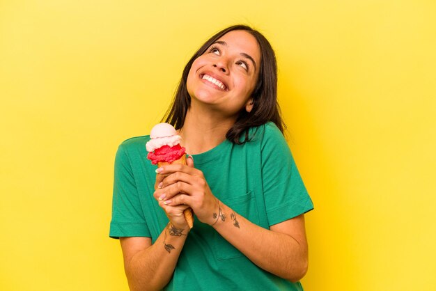 Joven hispana comiendo un helado aislado de fondo amarillo