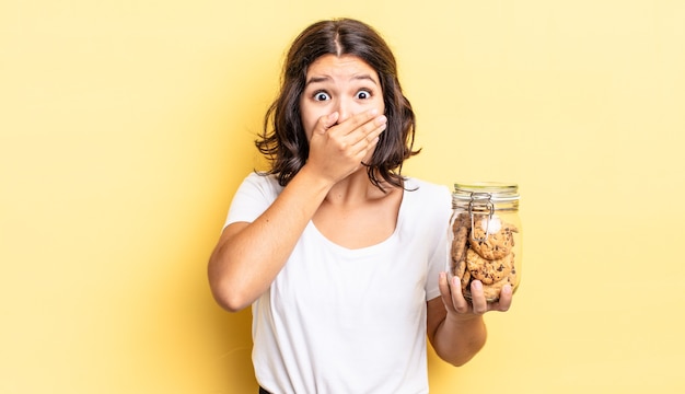 joven hispana cubriendo la boca con las manos con una sorpresa. concepto de botella de galletas