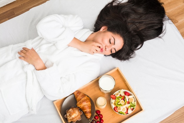 Joven hispana desayunando en la cama