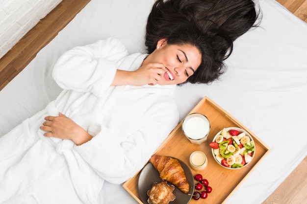 Joven hispana desayunando en la cama