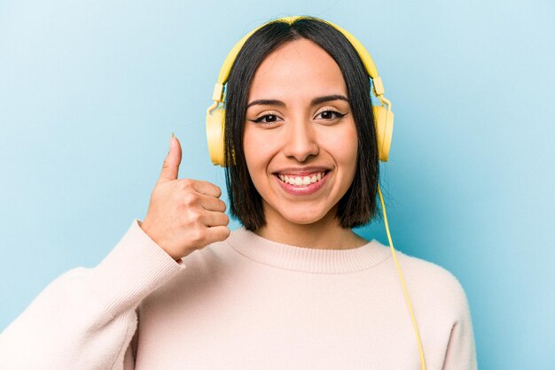 Joven hispana escuchando música aislada de fondo azul