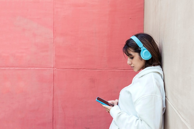 Joven hispana escuchando música con auriculares mientras usa el teléfono móvil al aire libre