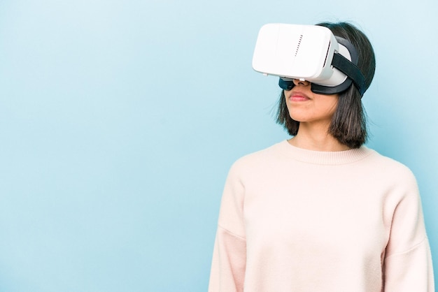 Joven hispana con gafas virtuales aisladas de fondo azul