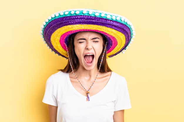 Joven hispana gritando agresivamente, luciendo muy enojada. concepto de sombrero mexicano