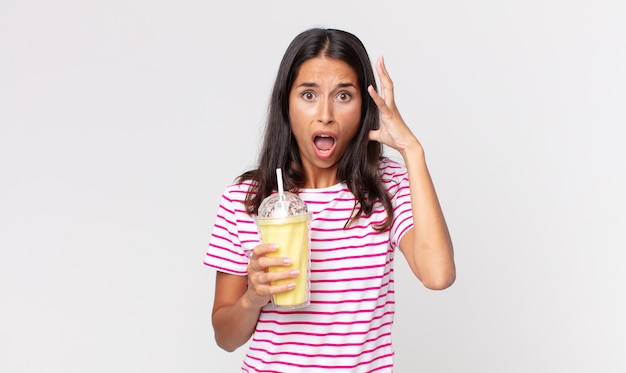 Joven hispana gritando con las manos en el aire y sosteniendo un batido de vainilla batido