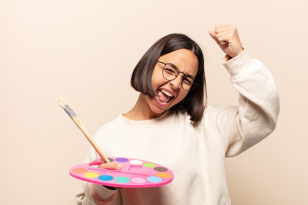 Foto joven hispana gritando triunfalmente, con aspecto de ganador emocionado, feliz y sorprendido