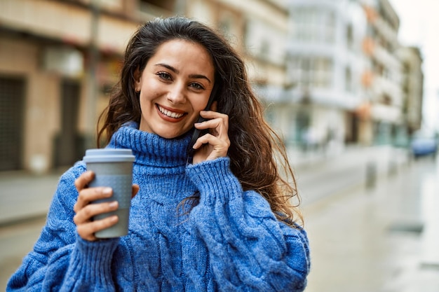 Joven hispana hablando por teléfono inteligente y tomando café en la ciudad