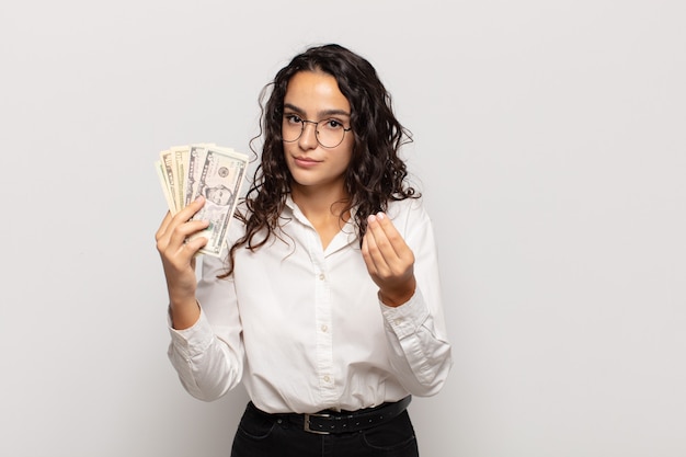 Joven hispana haciendo gesto de capice o dinero, ¡diciéndole que pague sus deudas!