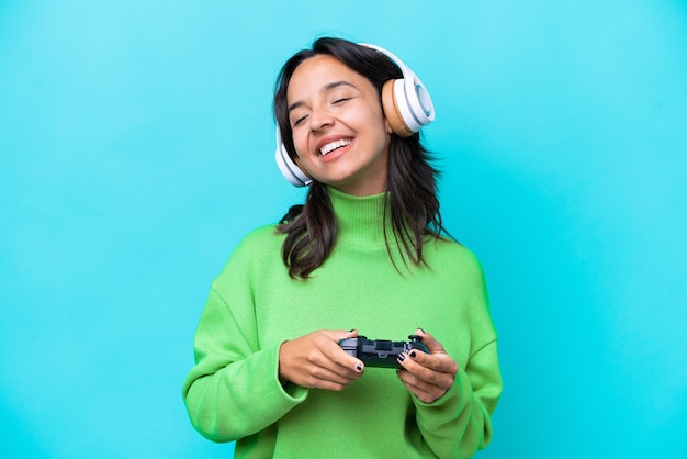 Joven hispana jugando con un controlador de videojuegos aislado de fondo azul riendo