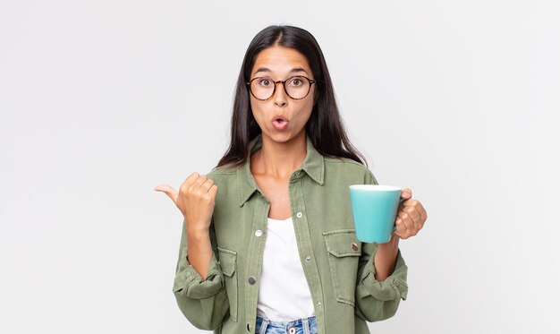 Joven hispana mirando asombrado con incredulidad y sosteniendo una taza de café