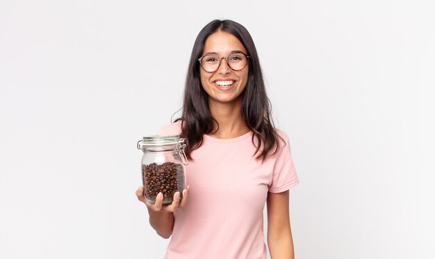 Joven hispana mirando feliz y gratamente sorprendido y sosteniendo una botella de granos de café