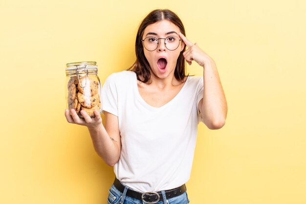 Joven hispana mirando sorprendido, dándose cuenta de un nuevo pensamiento, idea o concepto. concepto de botella de galletas