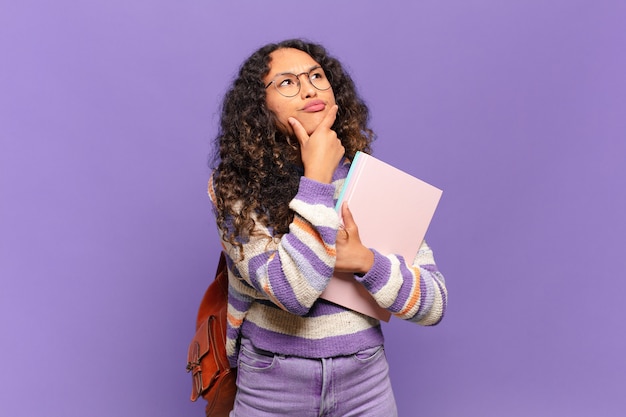 Joven hispana pensando, sintiéndose dudosa y confundida, con diferentes opciones, preguntándose qué decisión tomar. concepto de estudiante