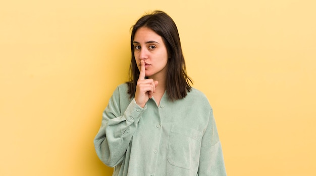 Joven hispana pidiendo silencio y silencio gesticulando con el dedo delante de la boca diciendo shh o guardando un secreto