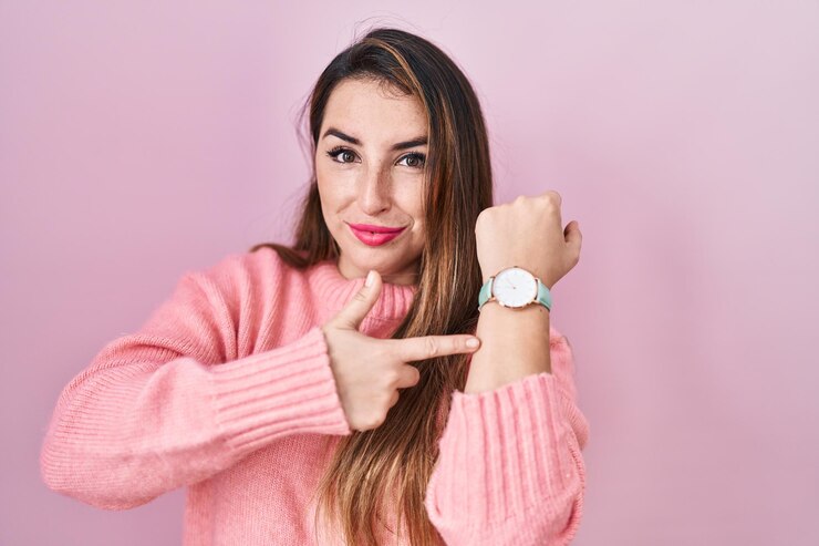 Foto joven hispana de pie sobre fondo rosa con prisa señalando el tiempo de reloj, impaciencia, mirando a la cámara con expresión relajada