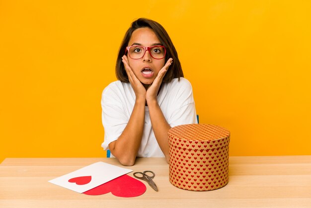 Joven hispana preparando un regalo de San Valentín aislado sorprendido y consternado.