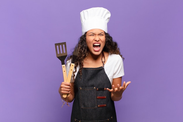 Joven hispana que parece enojada, molesta y frustrada gritando wtf o qué te pasa. concepto de chef de barbacoa