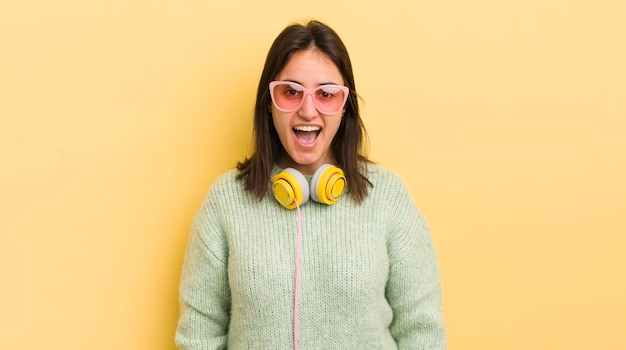 Foto joven hispana que parece feliz y gratamente sorprendida con el concepto de auriculares y gafas de sol