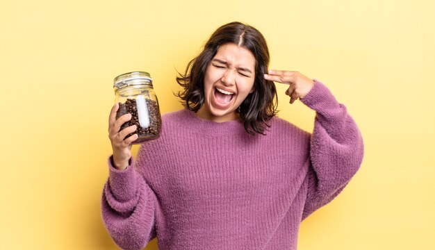 Joven hispana que parece infeliz y estresada, gesto de suicidio haciendo signo de pistola. concepto de granos de cafe