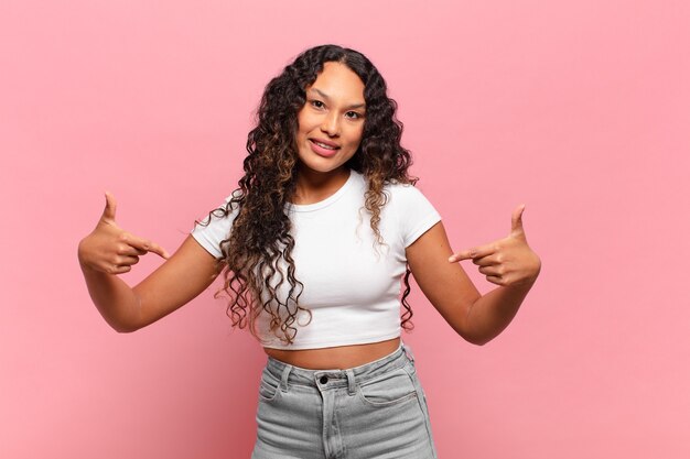 Foto joven hispana que parece orgullosa, arrogante, feliz, sorprendida y satisfecha, apuntando a sí misma, sintiéndose como una ganadora