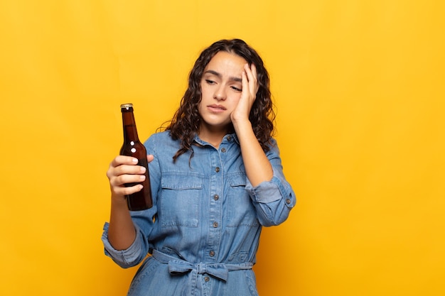 Joven hispana que se siente aburrida, frustrada y con sueño después de una tarea tediosa, aburrida y tediosa, sosteniendo la cara con la mano