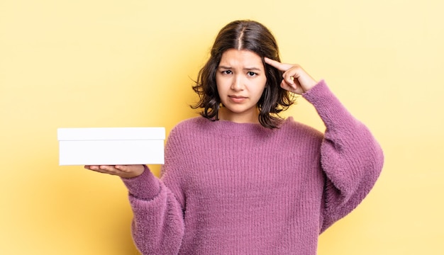 Joven hispana que se siente confundida y perpleja, mostrando que estás loco. concepto de caja en blanco