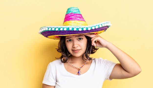 Foto joven hispana que se siente confundida y perpleja, mostrando que estás loco. concepto de sombrero mexicano
