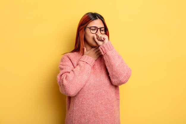 Joven hispana que se siente enferma con dolor de garganta y síntomas de gripe, tos con la boca cubierta