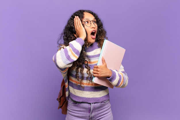 Joven hispana que se siente feliz emocionada y sorprendida mirando hacia un lado con ambas manos en la cara concepto de estudiante