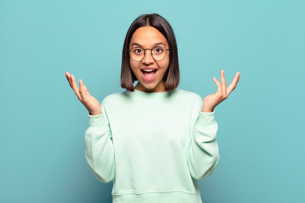 Joven hispana que se siente feliz, emocionada, sorprendida o conmocionada, sonriendo y asombrada por algo increíble