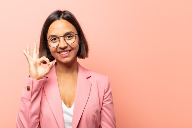 Joven hispana que se siente feliz, relajada y satisfecha, mostrando aprobación con gesto bien, sonriendo