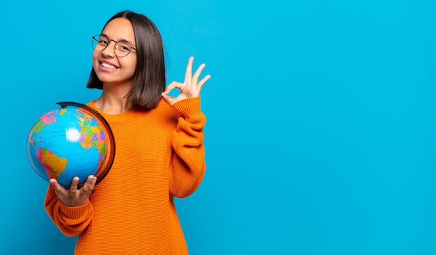 Joven hispana que se siente feliz, relajada y satisfecha, mostrando aprobación con gesto bien, sonriendo