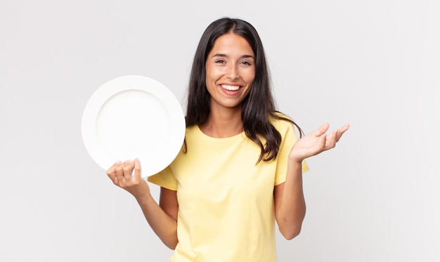 Joven hispana que se siente feliz, sorprendida al darse cuenta de una solución o idea y sosteniendo un plato vacío