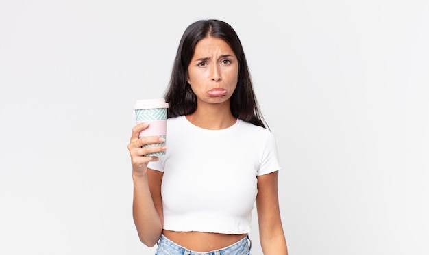 Foto joven hispana que se siente triste y llorona con una mirada infeliz y llorando y sosteniendo un recipiente de café para llevar