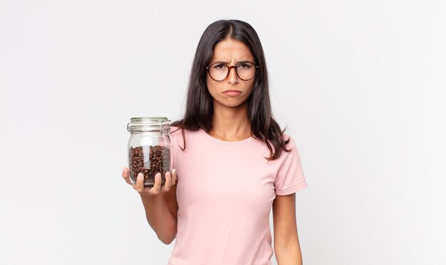 Joven hispana que se siente triste, molesta o enojada y mirando hacia un lado y sosteniendo una botella de granos de café