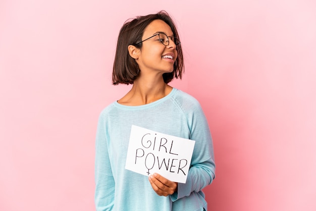 Foto joven hispana de raza mixta sosteniendo un cartel de mensaje de poder femenino mira a un lado sonriente, alegre y agradable.