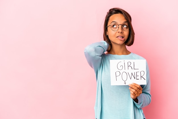 Joven hispana de raza mixta sosteniendo un cartel de mensaje de poder femenino tocando la parte posterior de la cabeza, pensando y tomando una decisión.