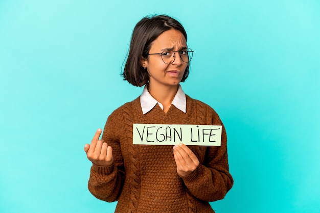 Joven hispana de raza mixta sosteniendo un cartel de vida vegana apuntando con el dedo como si invitara a acercarse.