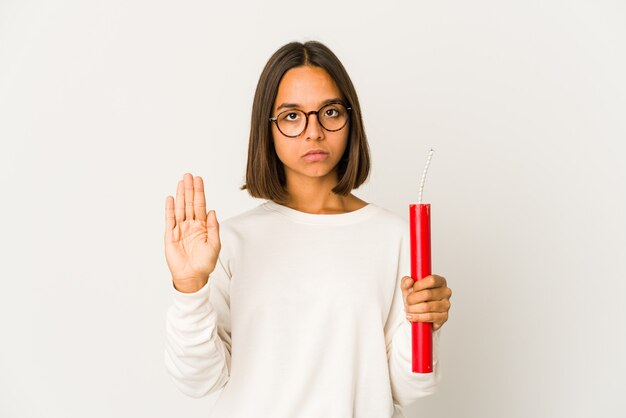 Joven hispana de raza mixta sosteniendo una dinamita de pie con la mano extendida mostrando la señal de stop, impidiéndote.