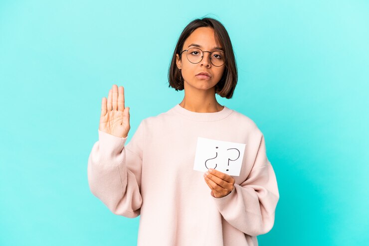 Foto joven hispana de raza mixta sosteniendo un tablero de interrogatorio de pie con la mano extendida mostrando la señal de stop, impidiéndote.