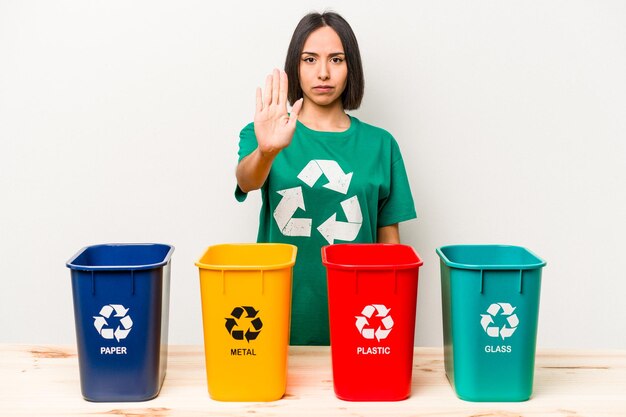 Foto joven hispana reciclando aislada de fondo blanco de pie con la mano extendida mostrando la señal de stop que te impide