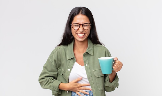 Joven hispana riendo a carcajadas de una broma hilarante y sosteniendo una taza de café