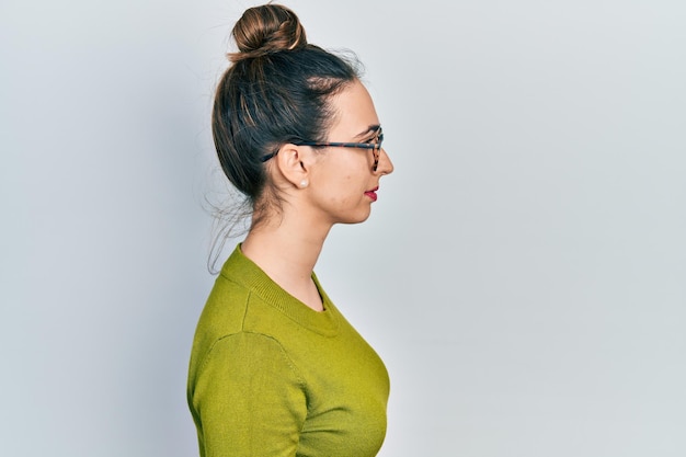 Joven hispana con ropa informal y anteojos mirando hacia un lado, relaja la pose de perfil con rostro natural con una sonrisa segura.