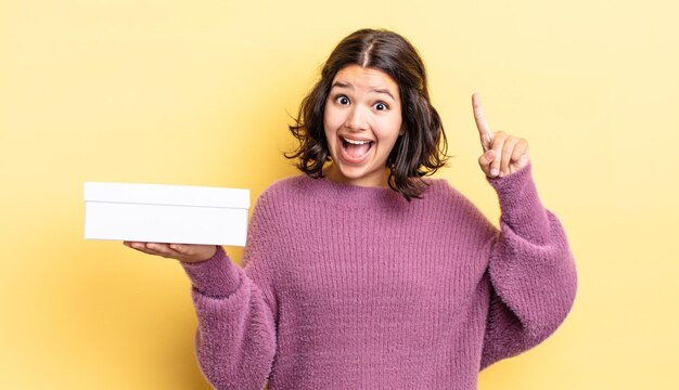 Joven hispana sintiéndose como un genio feliz y emocionado después de realizar una idea. concepto de caja en blanco