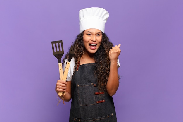 Joven hispana sintiéndose conmocionada, emocionada y feliz, riendo y celebrando el éxito, diciendo ¡guau !. concepto de chef de barbacoa