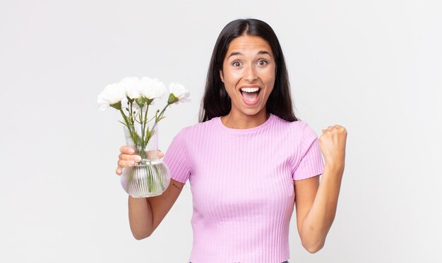 Joven hispana sintiéndose conmocionada, riendo y celebrando el éxito sosteniendo flores decorativas